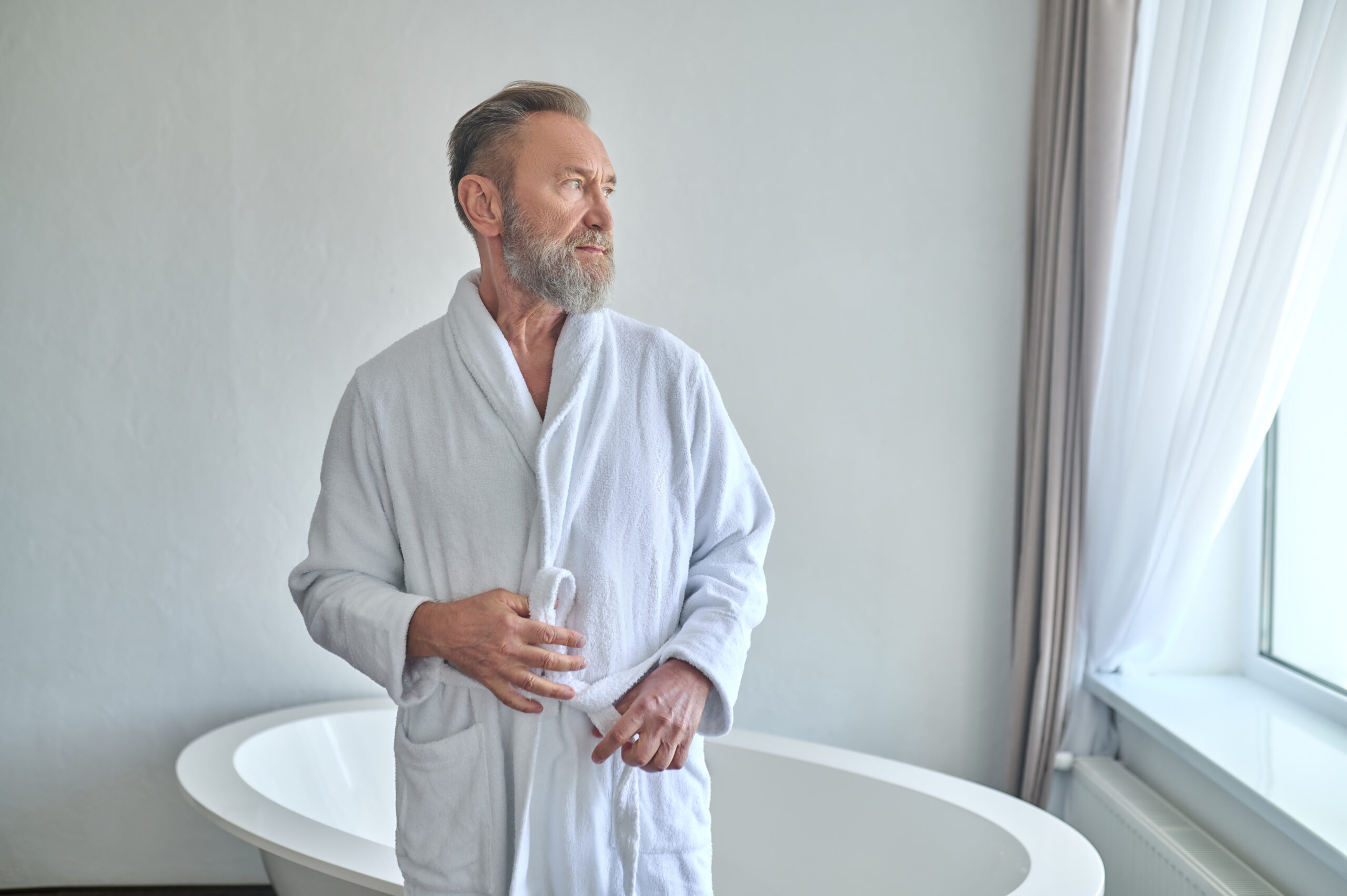 Elderly man in robe preparing to take a bath.