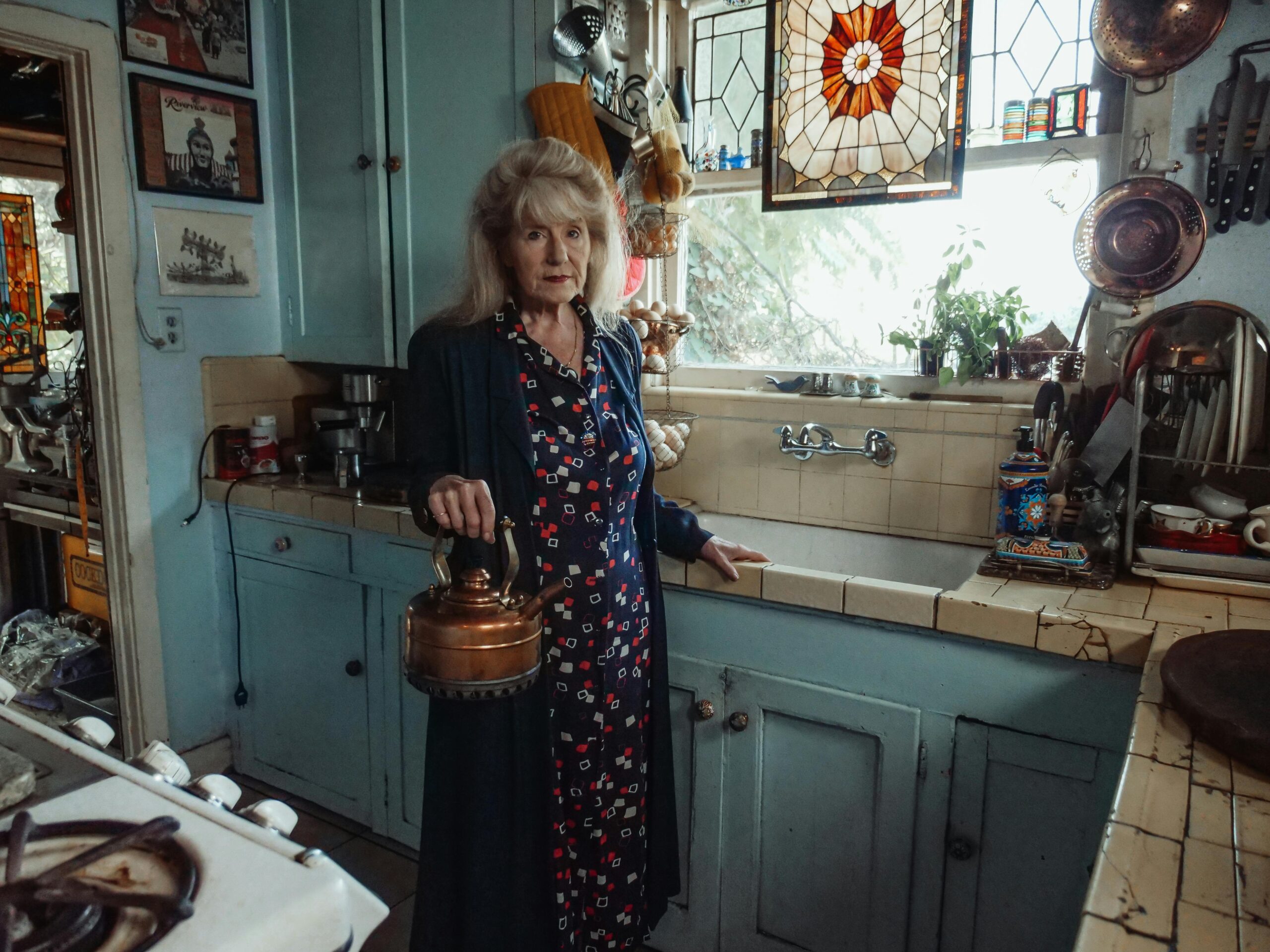 Elderly women in kitchen holding a tea kettle. 